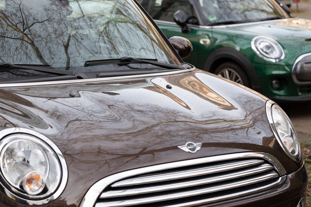 Close-up of two Mini Cooper cars reflecting urban surroundings, emphasizing modern design.